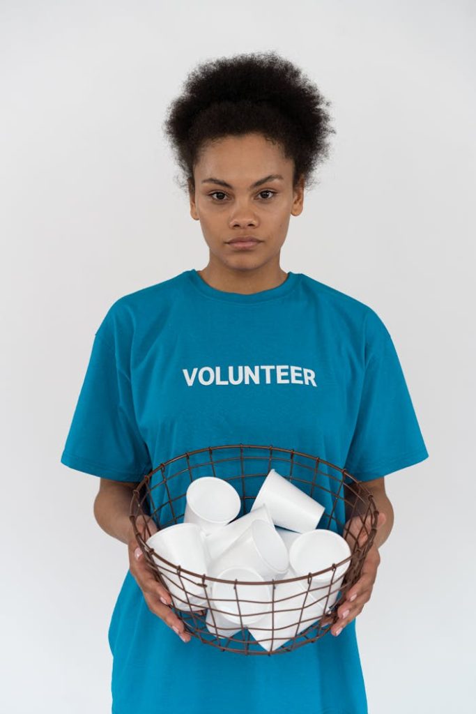 a-woman-wearing-a-blue-shirt-holding-a-metal-basket-7475051 African American volunteer holding a basket of disposable cups, promoting environmental conservation.
